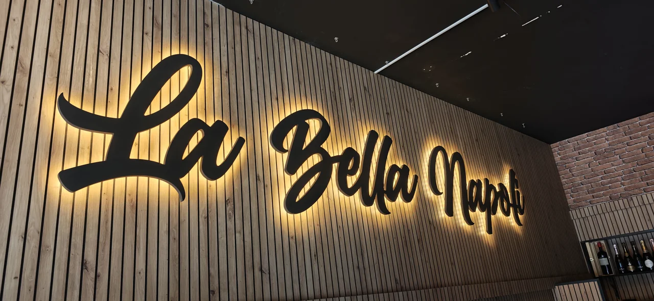 Letras de La Bella Napoli con un halo de luz sobre un revestimiento de listones.